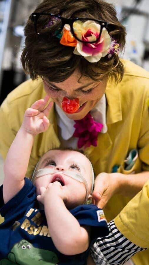 Dr Maybe looks down at a toddler who is looking back up at her and reaching for her nose.