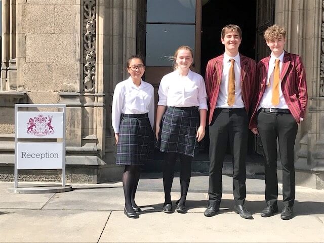 Four secondary school students stand outside their school