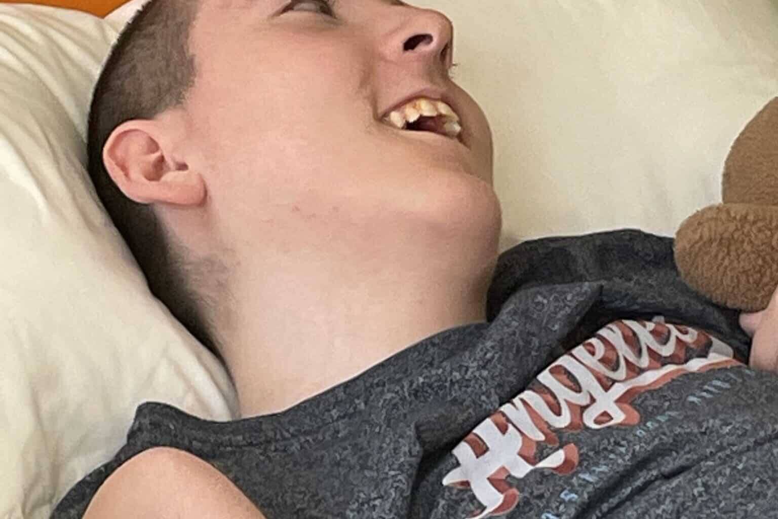 A teenage boy reclines in bed with a huge smile on his face