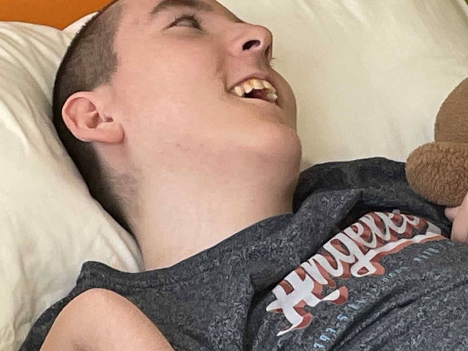A teenage boy reclines in bed with a huge smile on his face